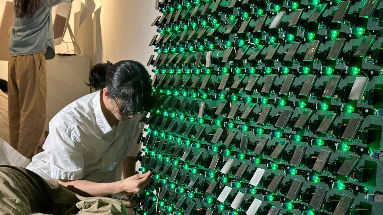 A team member attaching mirrors behind a wall dotted with green lights.