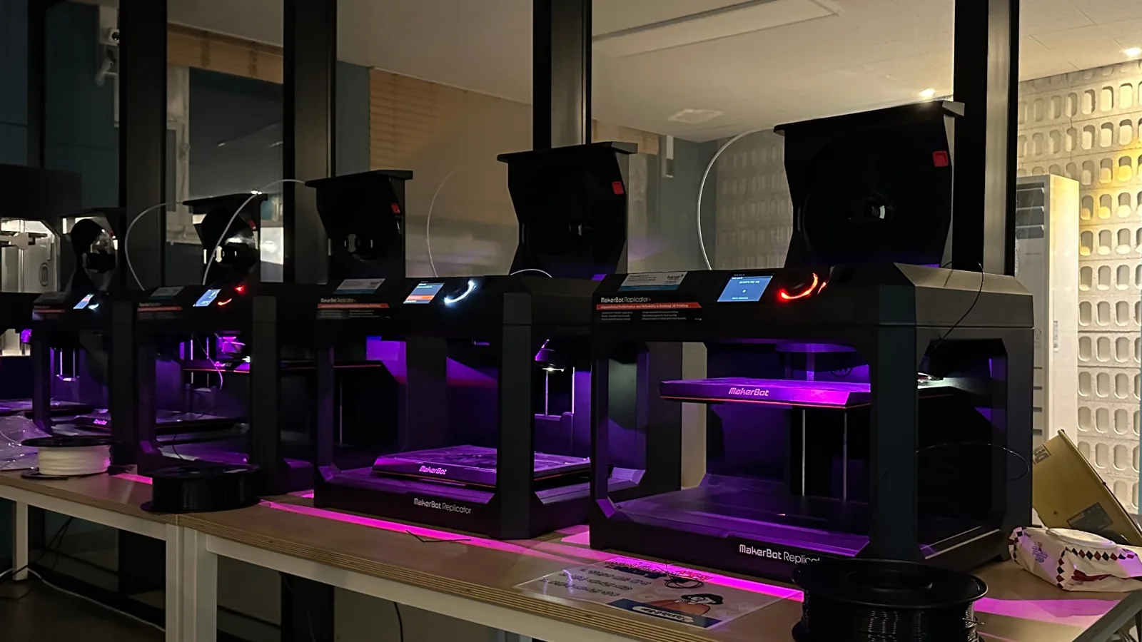 Five 3D printers under purple light running side by side.
